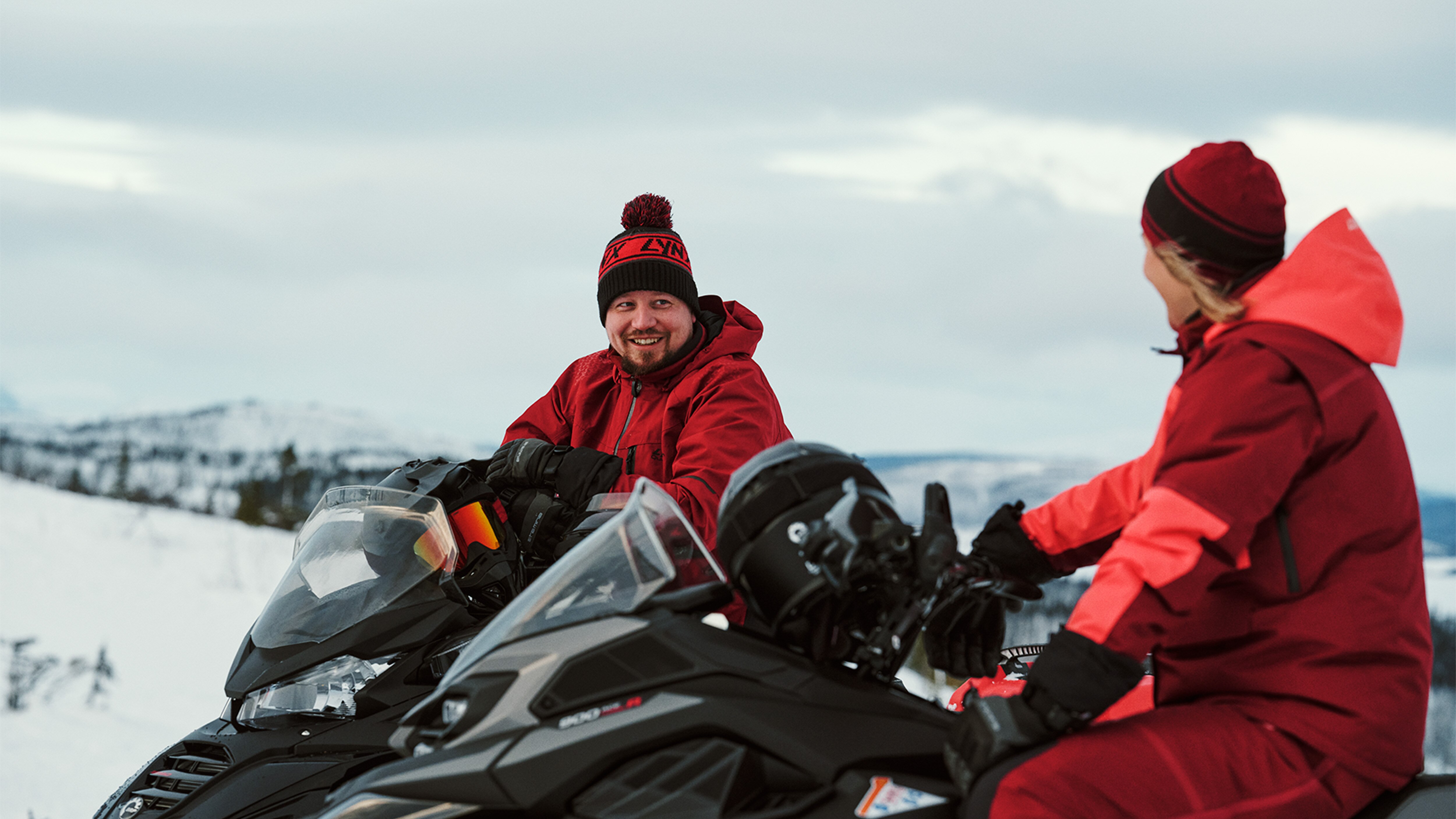 Man and woman chatting on Lynx Brutal RE 2025 snowmobiles
