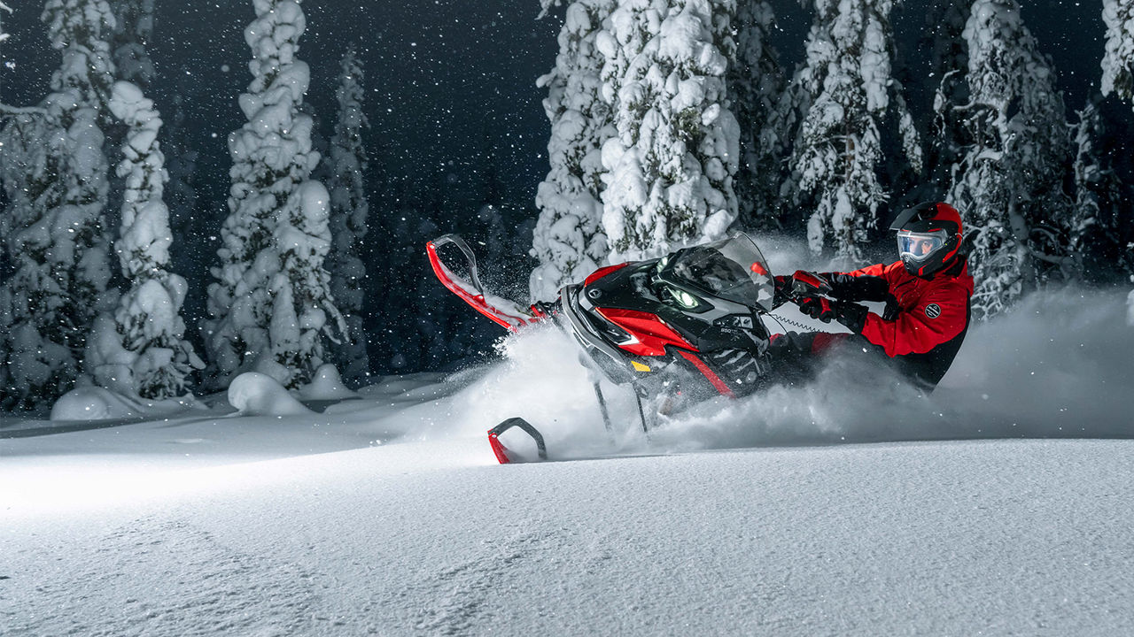 Lynx Xterrain RE -moottorikelkka kääntyy syvällä lumella pimeässä metsässä.