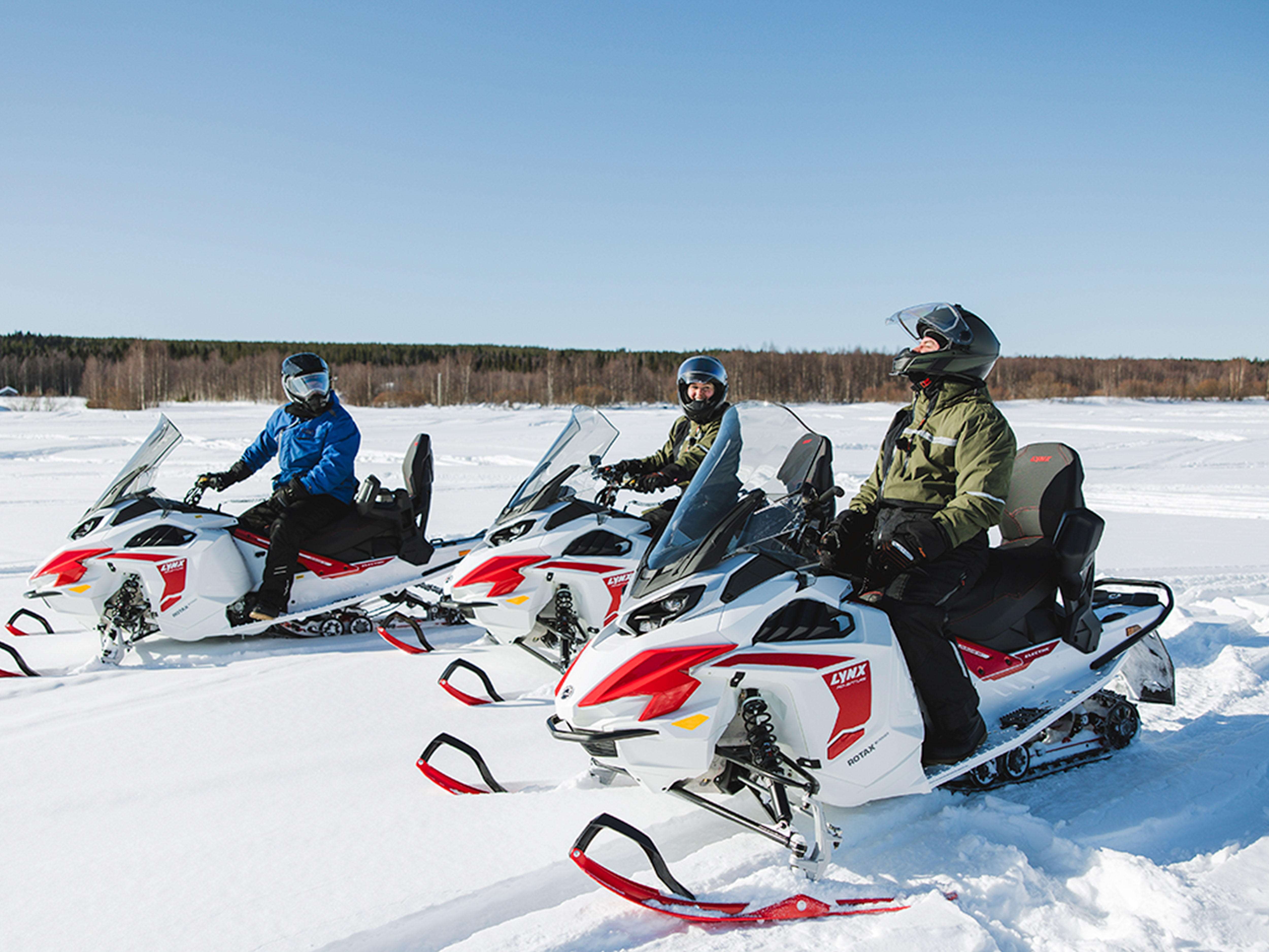 Three riders chatting on Lynx Adventure Electric snowmobiles on the lake ice