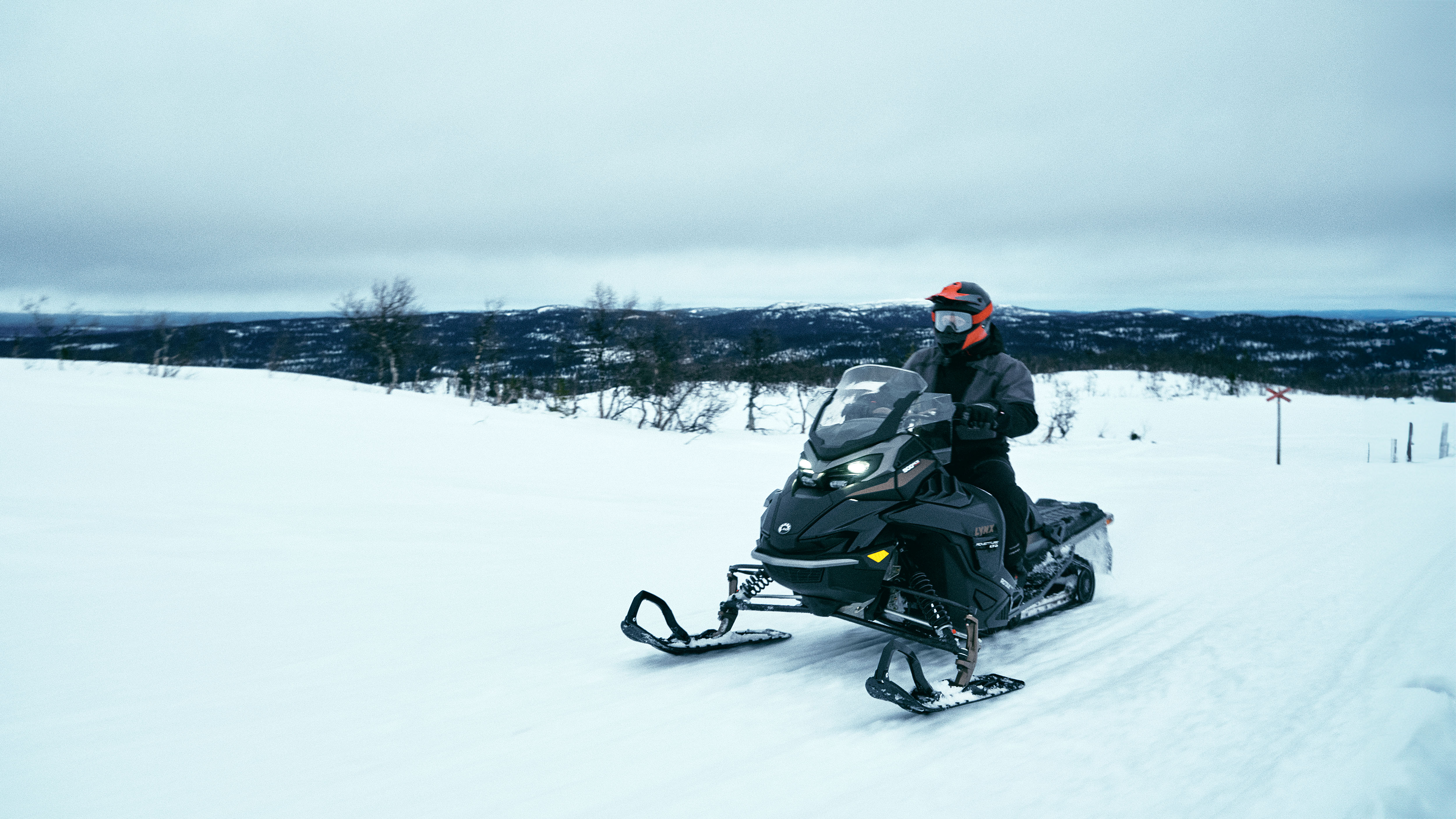 2025 Lynx Trail snowmobile riding up a snowy trail.