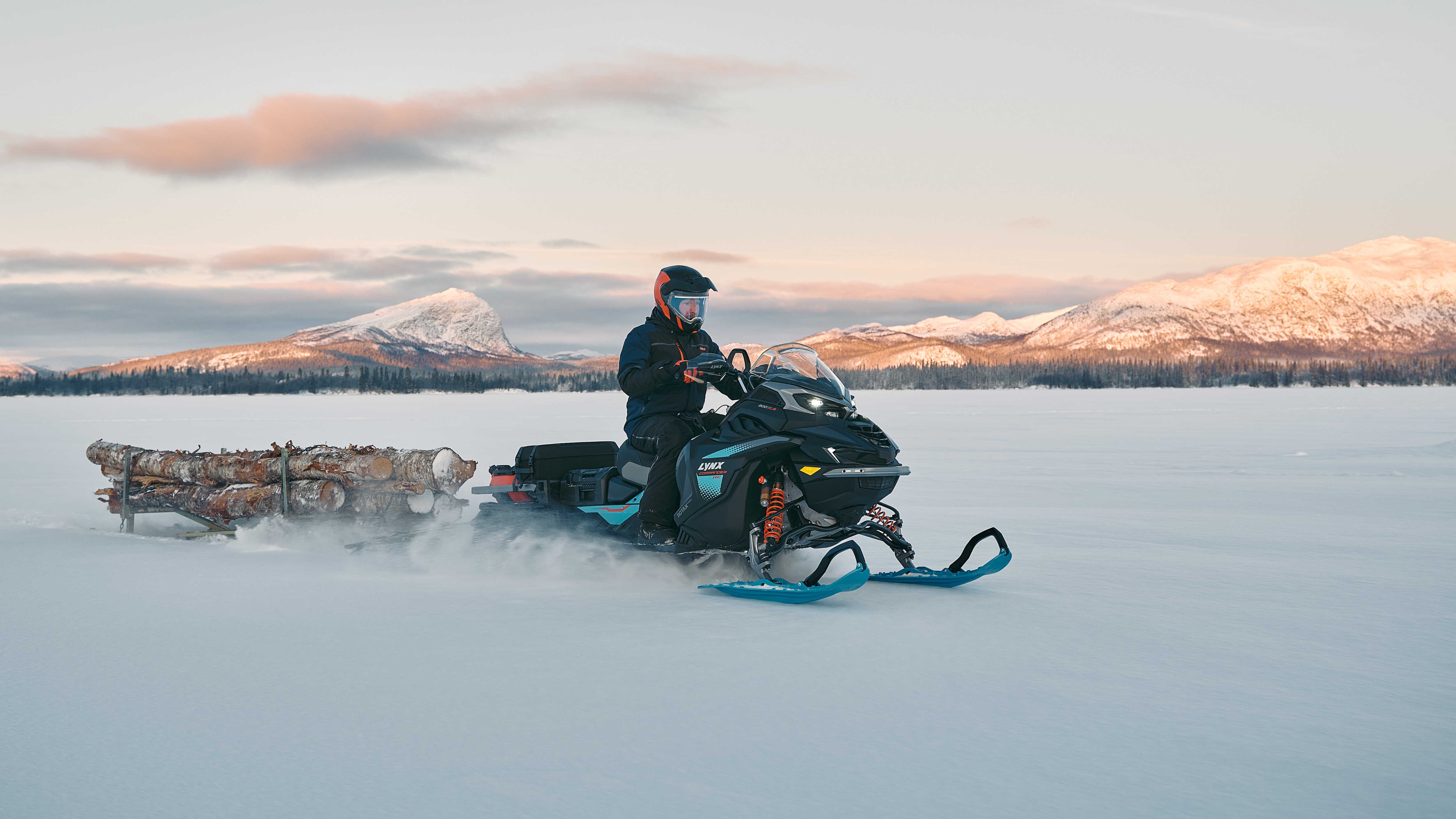 Snowmobiler hauling tree trunks in a trailer behind his 2026 Lynx Commander snowmobile.