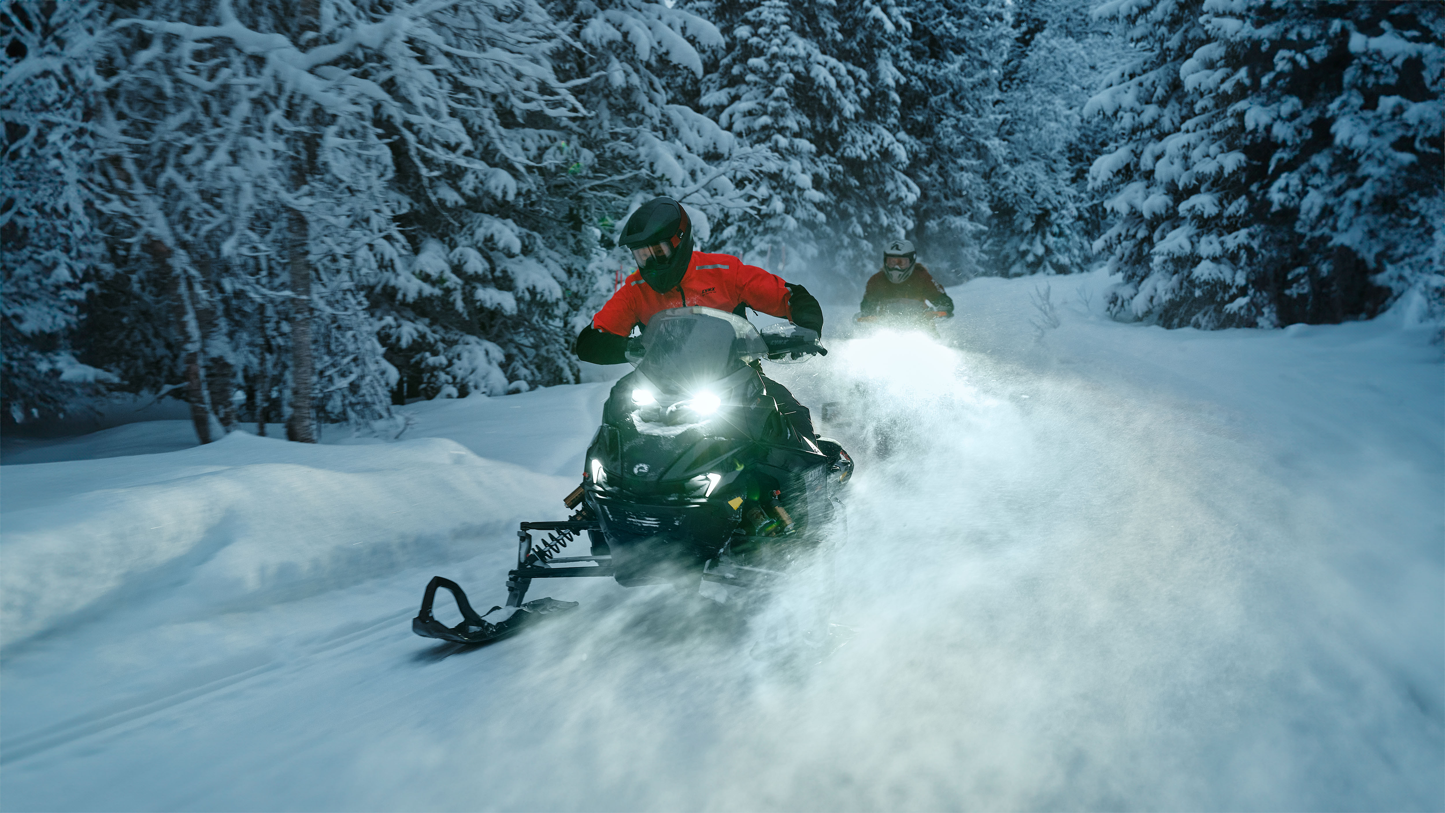 Deux motoneigistes sur leur motoneige Lynx Rave RE 2026 parcourant une piste enneigée en forêt.