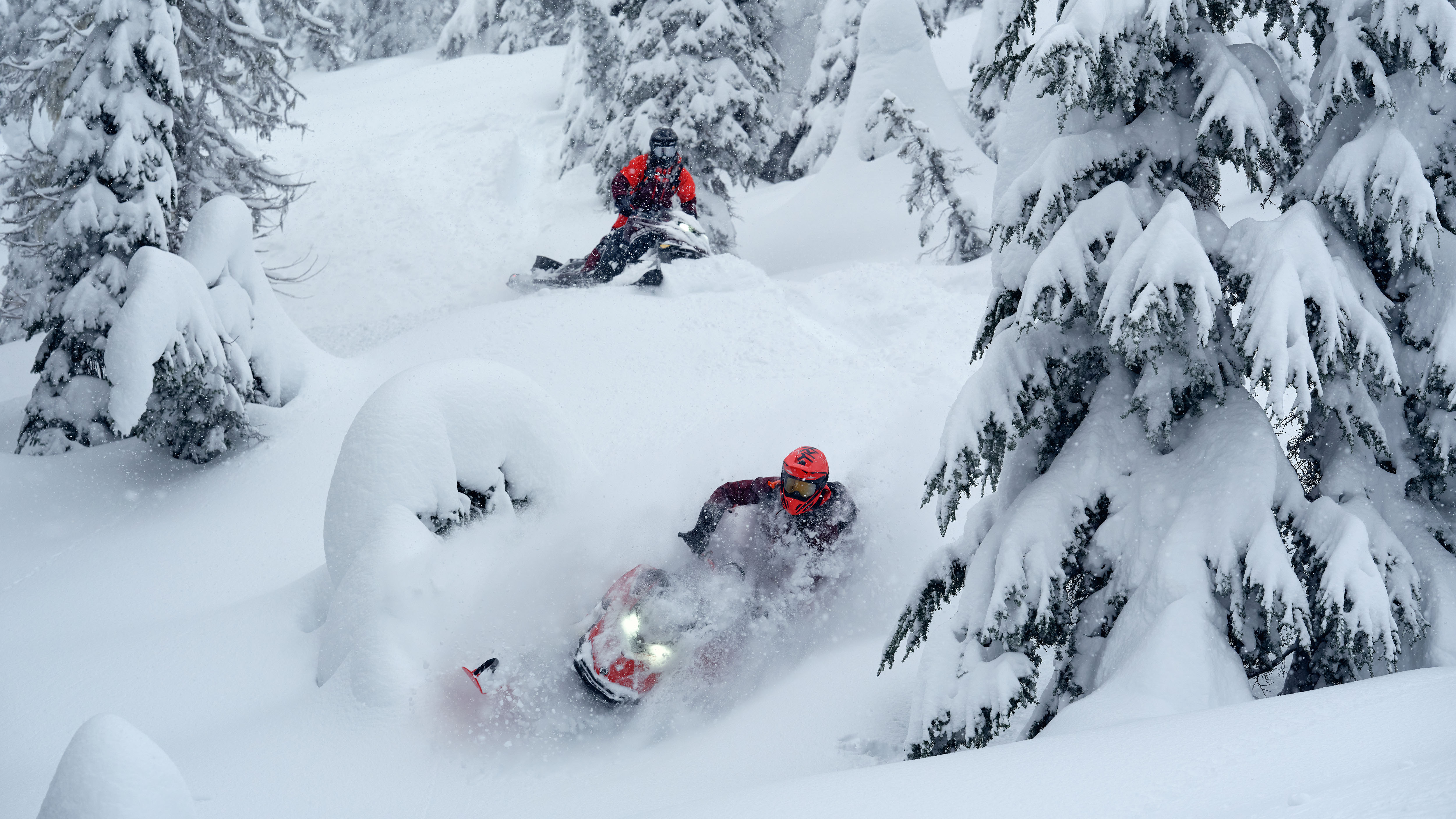 Two snowmobilers riding their 2026 Lynx Shredder snowmobile through the deep snow of a snow-covered forest.