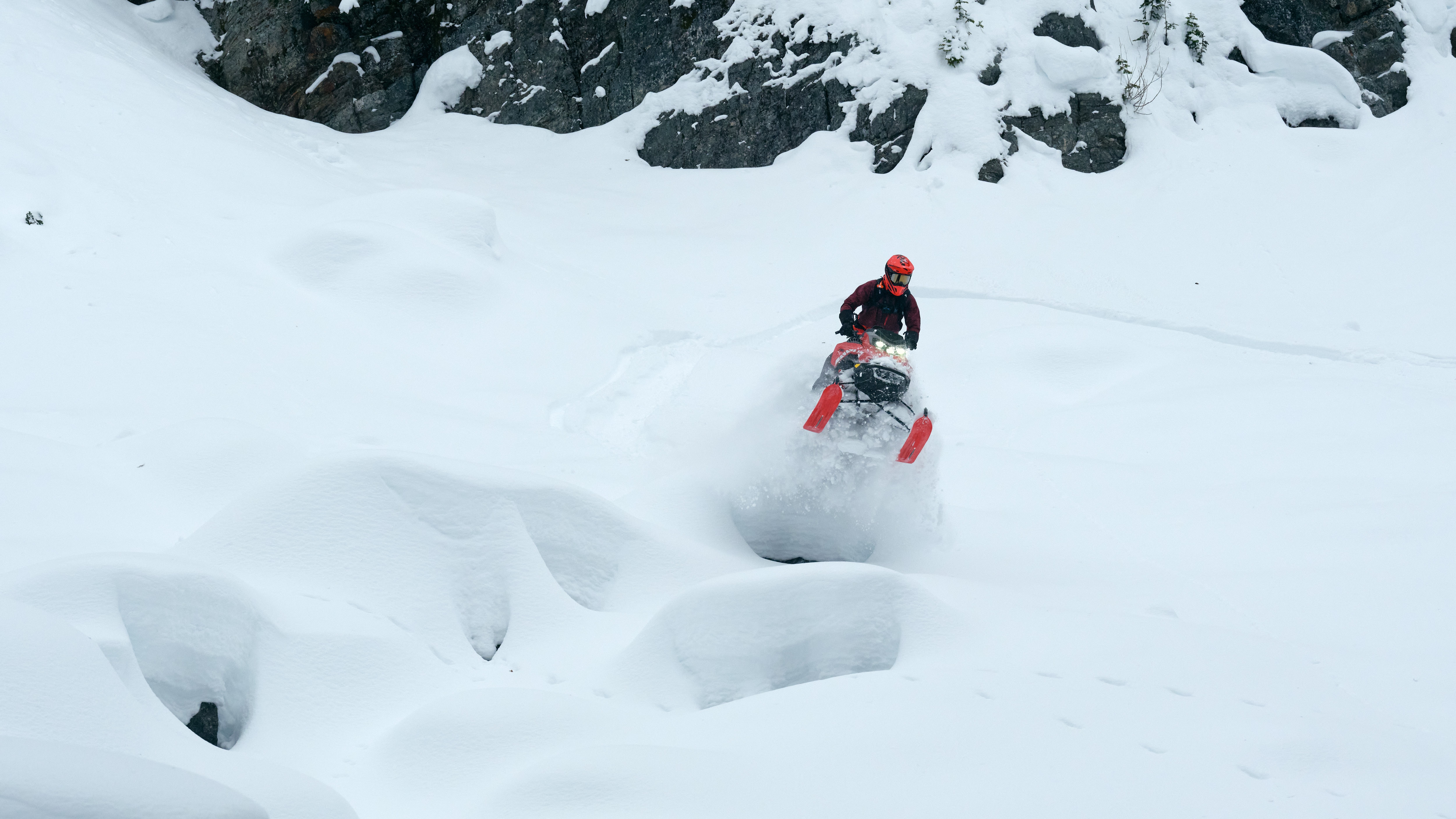 Snowmobiler making a jump with a 2026 Lynx Shredder RE snowmobile on a snow-covered mountain.