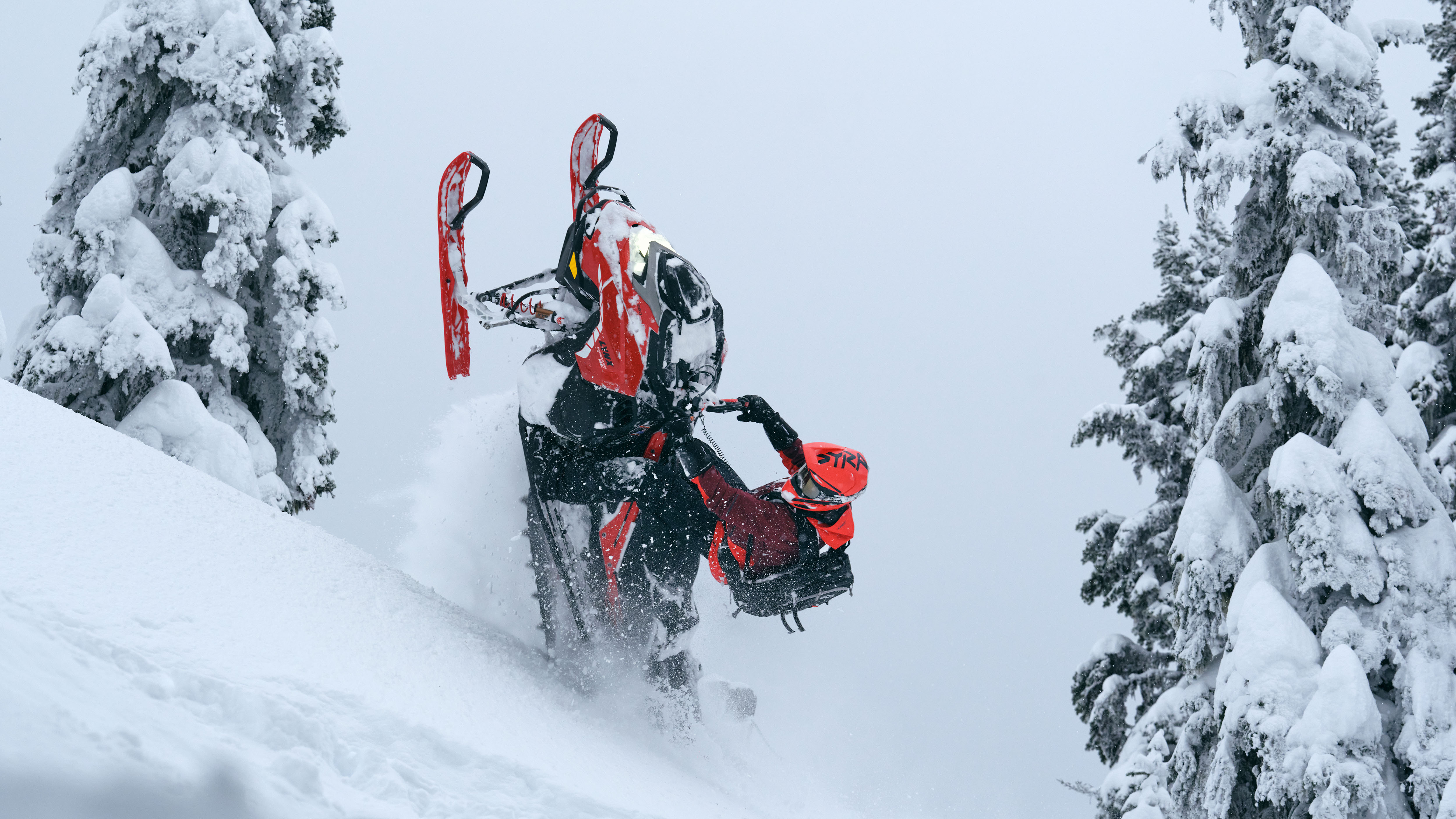 Rider performing a trick on a 2026 Lynx Shredder snowmobile in a snow-covered forest.