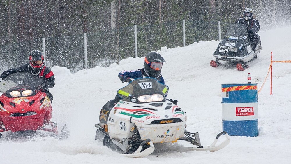 Vintage snowcross snowmobiles Lynx and Ski-Doo ride corner on a race track. 