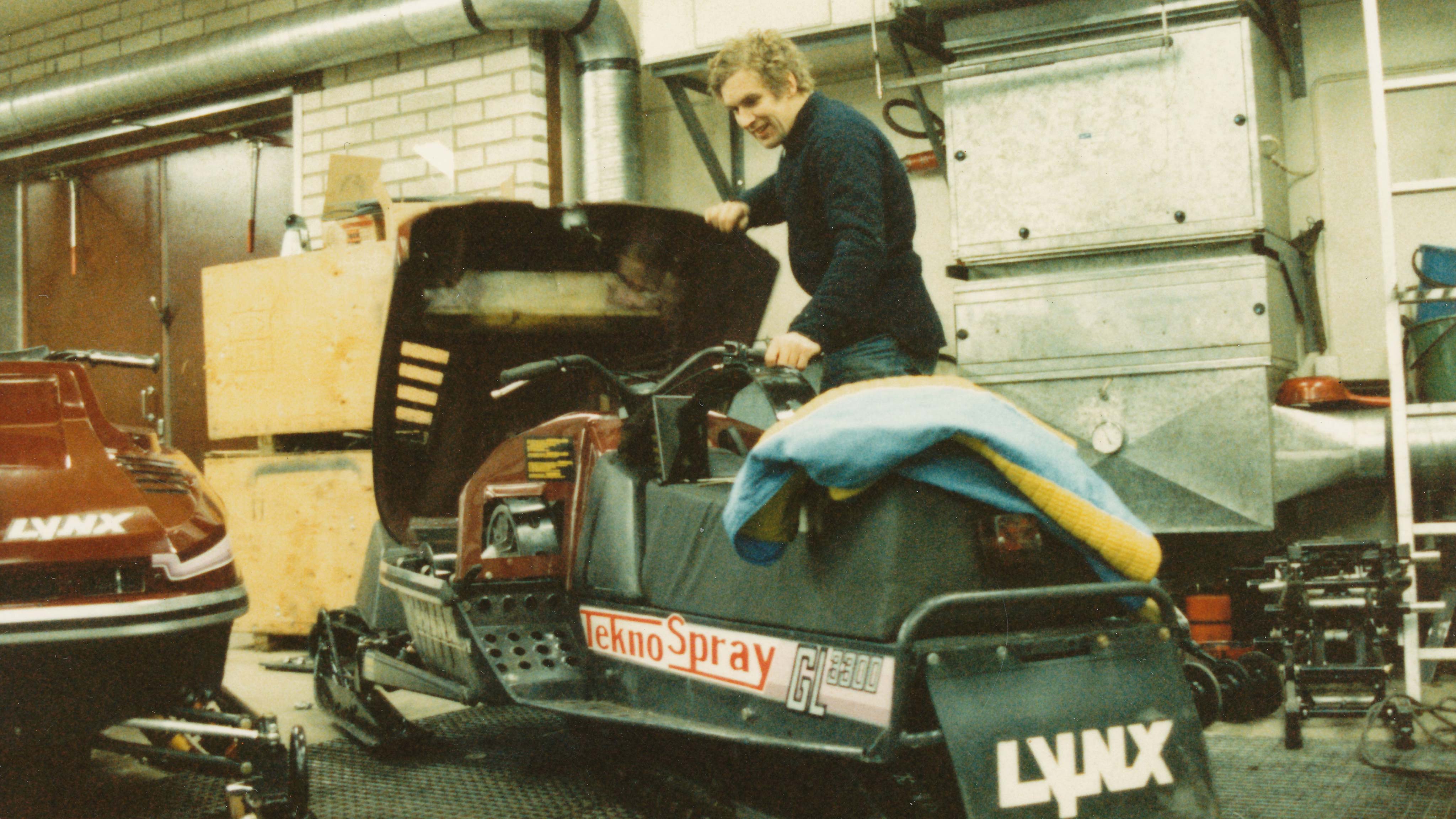 Mies avaamassa vanhan Lynx kilpamoottorikelkan kuomua verstaassa