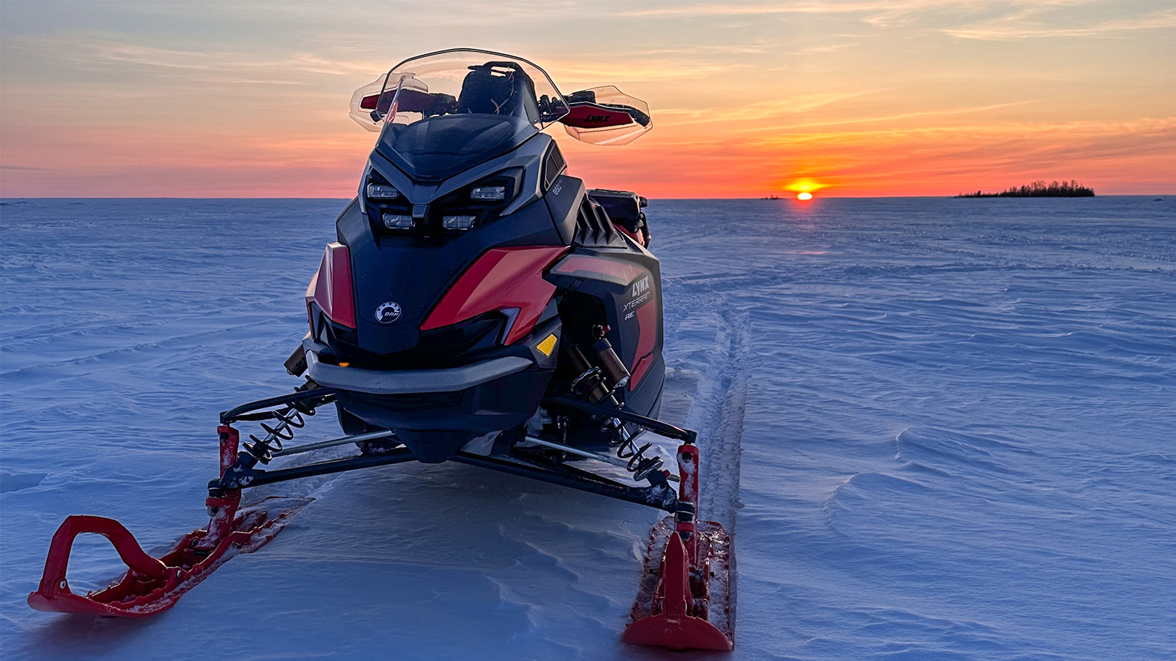Lynx Xterrain RE 850 E-TEC crossover snowmobile parked on a frozen lake at sunset