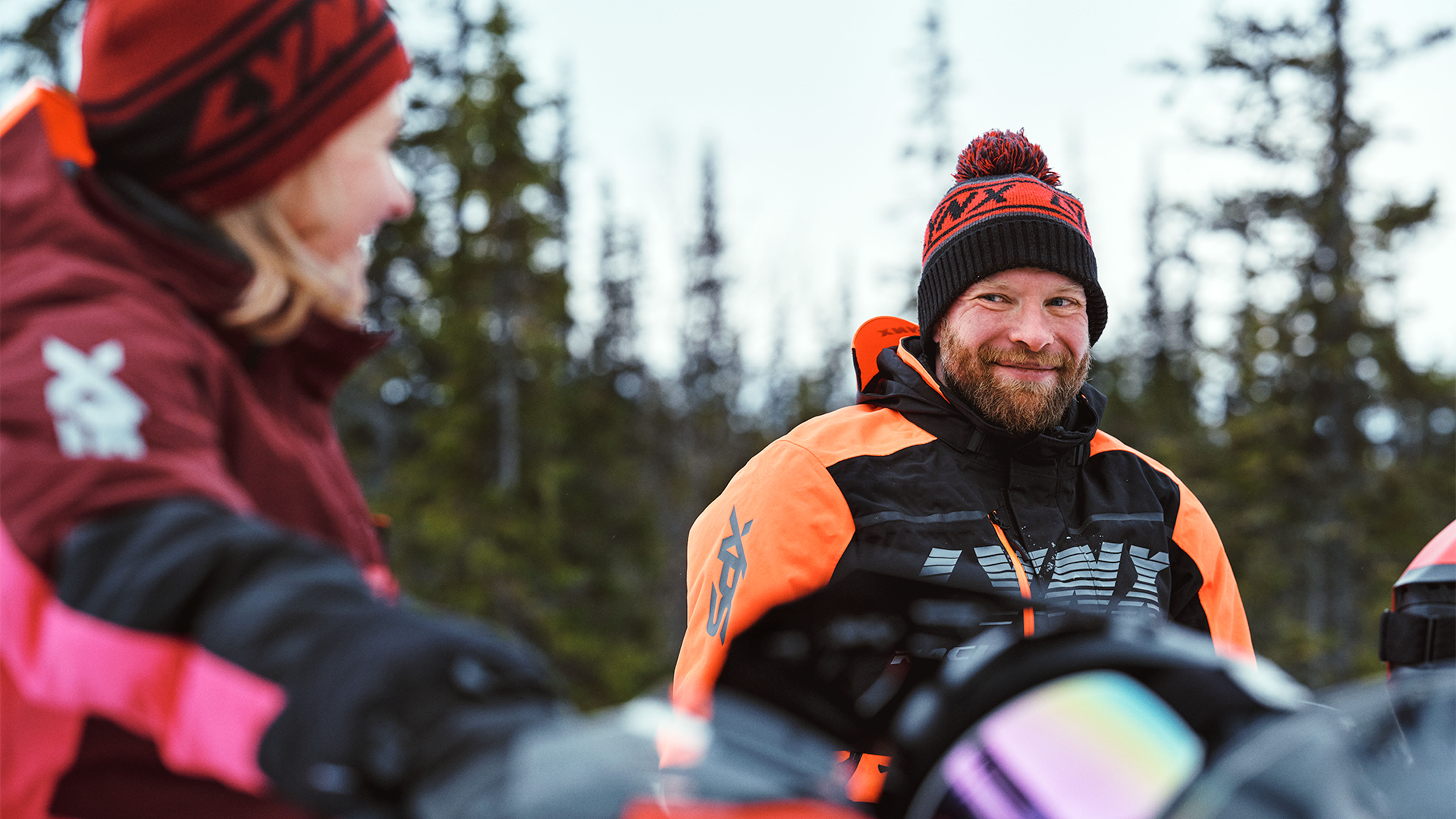 Woman and man chatting on snowmobiles in Lynx riding apparel